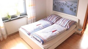 Un letto singolo con lenzuola a righe, una finestra con tende, un termosifone e un quadro appeso al muro.