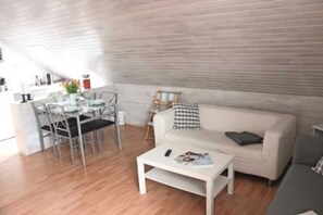 A modern living room with a white sofa, a coffee table, and a dining area with chairs and a table.