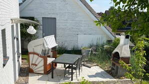 Un patio con un divano in vimini, un tavolo, sedie, una pianta in vaso e un barbecue in pietra.