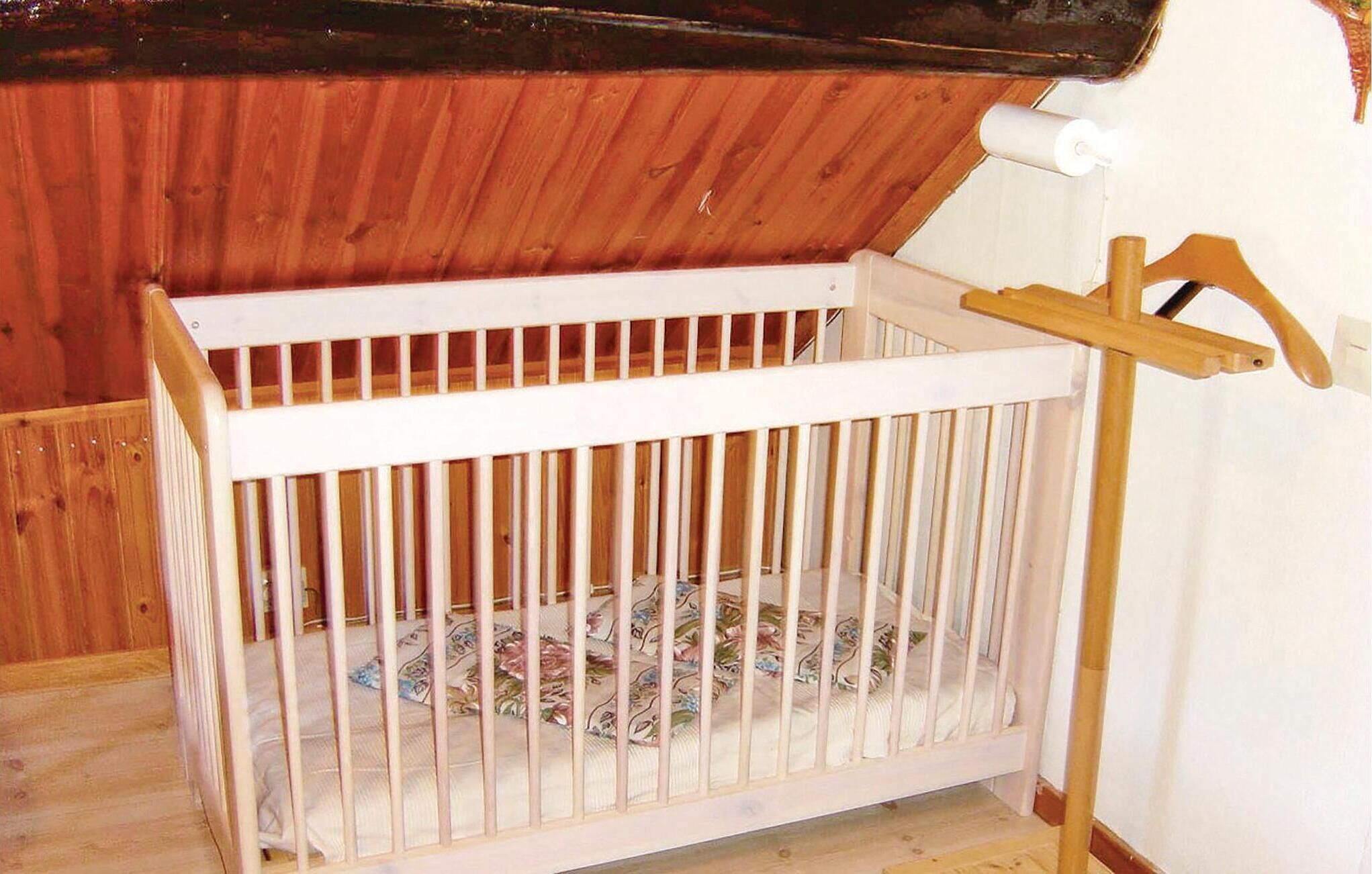 A white crib with a wooden frame, a wooden ladder, and a wooden ceiling.