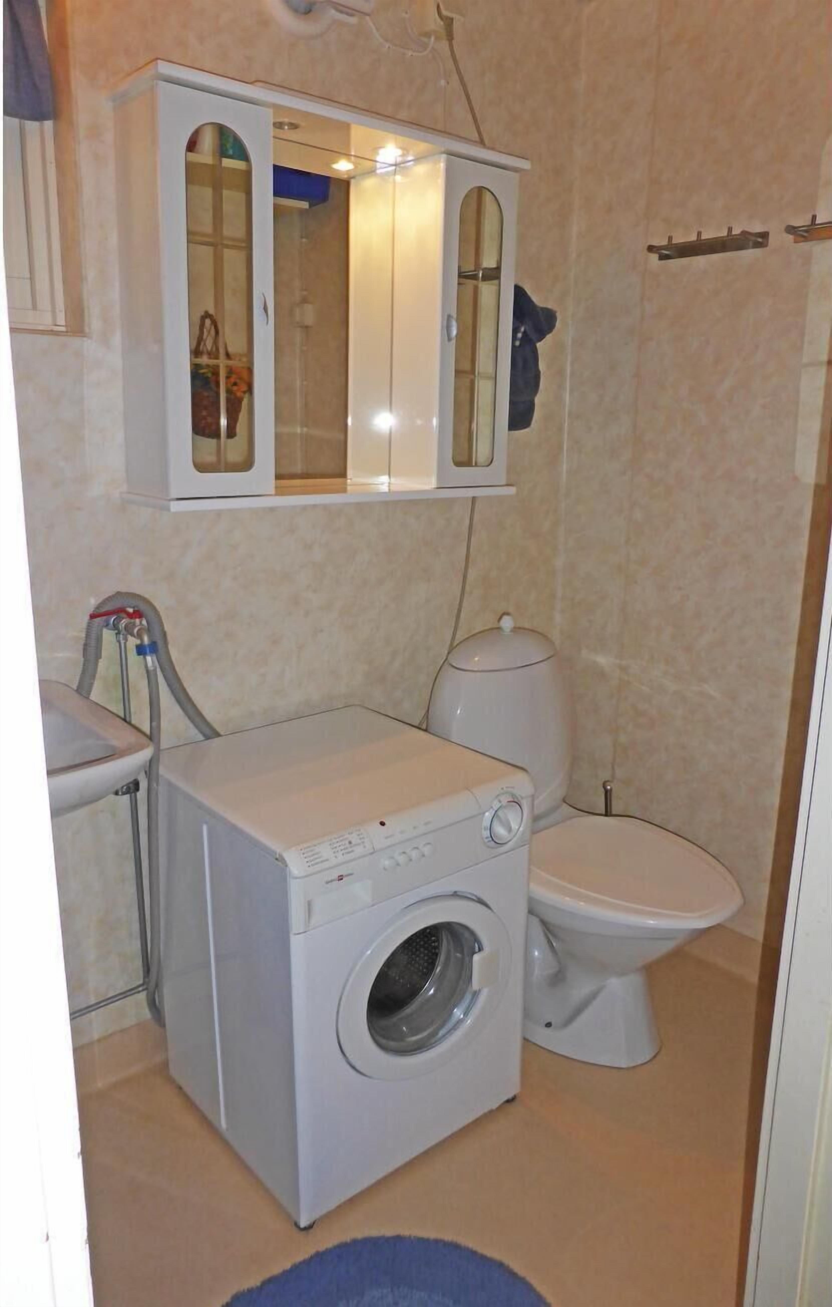 A compact bathroom with a washing machine, toilet, and a cabinet with a mirror.