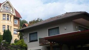 A two-story house with a garage, a covered driveway, and a car parked inside. - Vacation apartment Haus am Sonnenhang - Holiday apartment (Bad Sachsa)