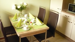 A dining area with a table set for two, a vase with flowers, and a microwave in the background. - Vacation apartment Haus am Sonnenhang - Holiday apartment (Bad Sachsa)