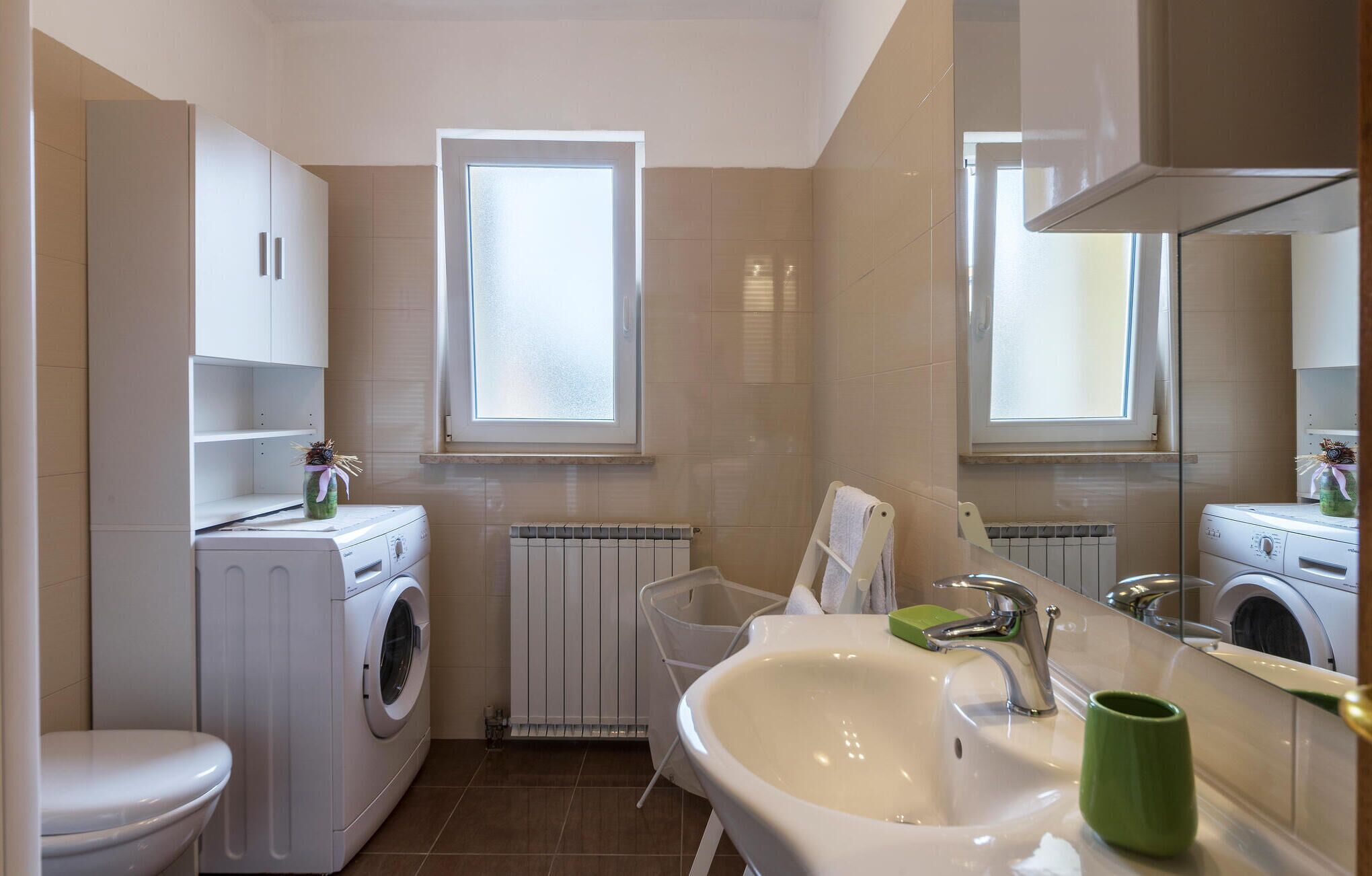 A modern bathroom with a toilet, washing machine, sink, and a large mirror.