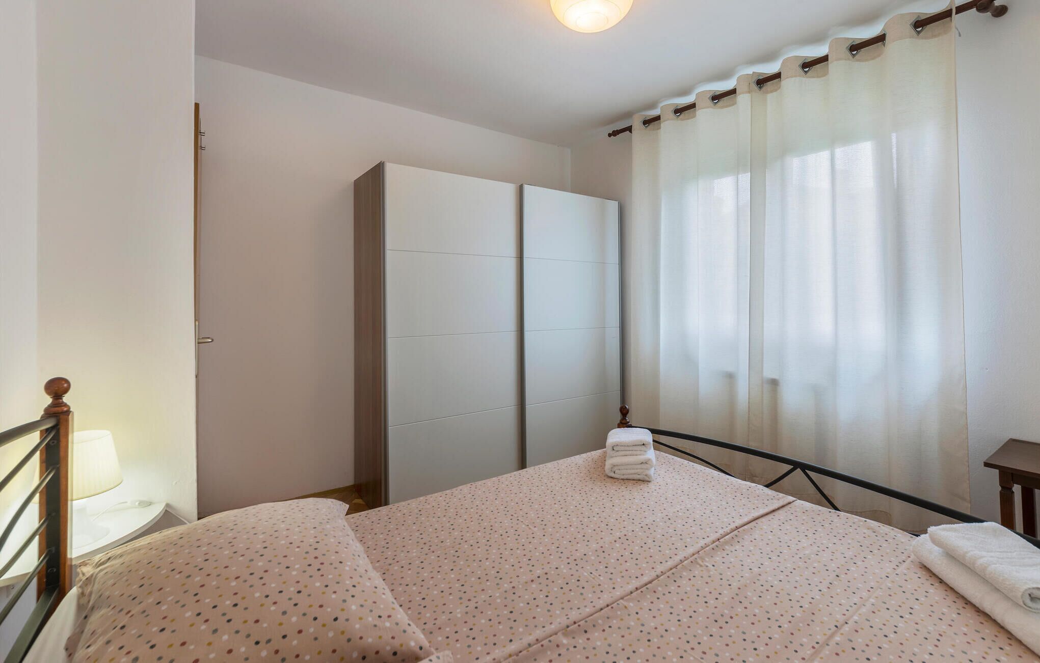 Une chambre à coucher avec un lit, une armoire, une table de chevet et une fenêtre avec des rideaux.