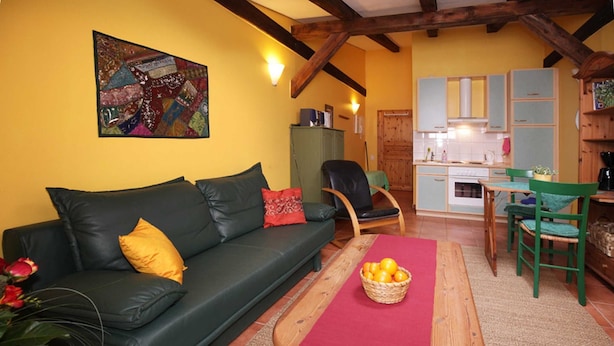 A cozy living room with a green sofa, a wooden coffee table with oranges, and a kitchen in the background. - Apartment 2 - The Mouse - Vacation at Duckwitz Castle (Behren-Lübchin)