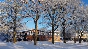 Paesaggio innevato con alberi spogli e un edificio in mattoni con una porta verde.