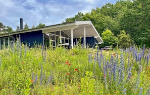 Ett modernt hus med en inglasad veranda, omgivet av en frodig trädgård med många olika vilda blommor.