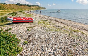 A red inflatable boat on a pebbly beach with a pier extending into the water. - Beautiful home in Knebel with WiFi (Knebel)