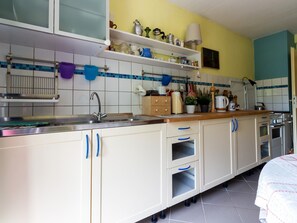 A kitchen with white cabinets, a sink, and a stove. There are shelves above the sink with various kitchen items.