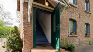 Un bâtiment en briques avec une porte verte et un escalier menant à l’intérieur.