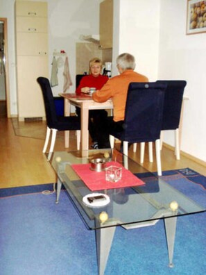 Een eetgedeelte met een tafel met glazen blad, stoelen en een rode placemat.