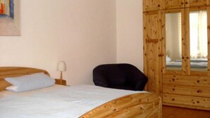 A bedroom with a bed, a chair, a wooden wardrobe, and a painting on the wall.