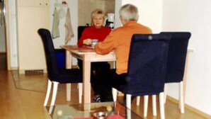 A dining area with a glass-top table, chairs, and a red placemat.