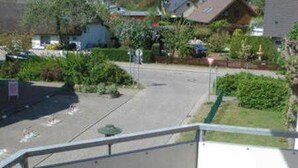 A residential street with houses, a clear sky, and a balcony with a metal railing.