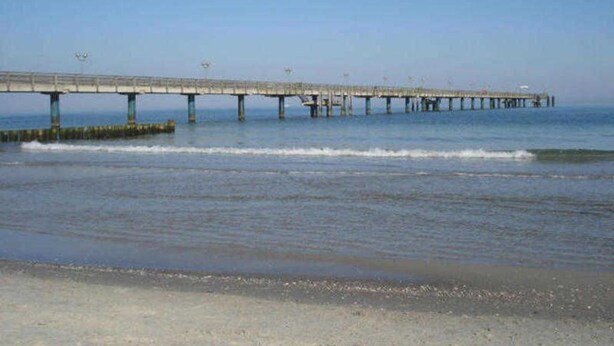 A long pier extending into the water with a clear sky above.