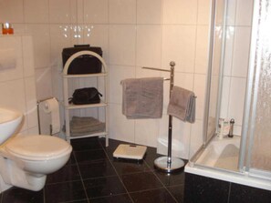 Un baño con inodoro, balanza, toallero y zona de ducha.