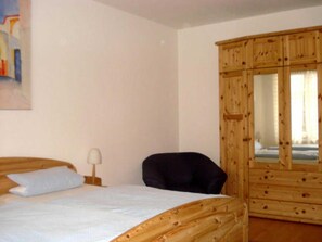 Een slaapkamer met een bed, een stoel, een houten garderobe en een schilderij aan de muur.