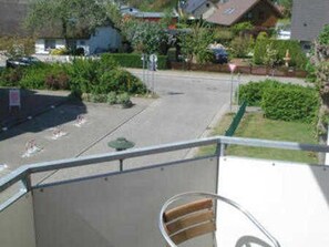 Una calle residencial con casas, cielo despejado y un balcón con barandilla metálica.