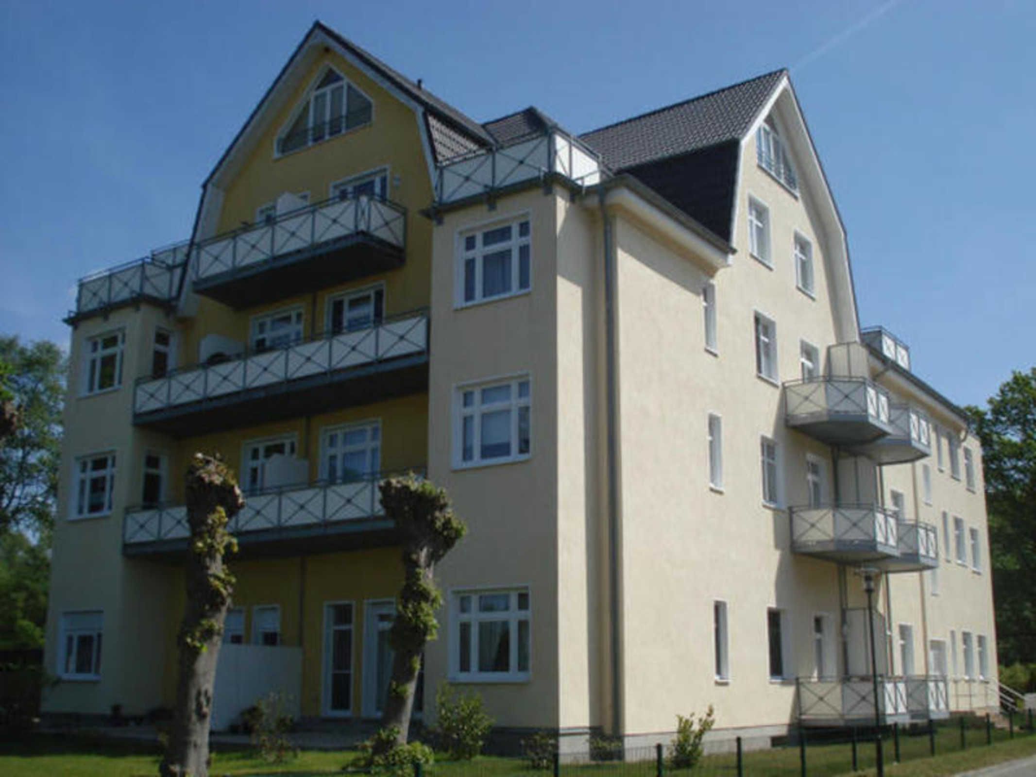 Ein mehrstöckiges Gebäude mit Balkonen, einer flachen Dachterrasse und einer symmetrischen Fassade.