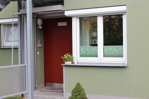 Une maison avec une porte rouge, un petit porche et une fenêtre avec des stores.