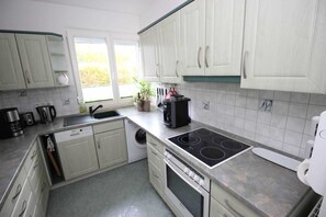 Une cuisine moderne avec des armoires blanches, un lave-vaisselle intégré, une cuisinière et une machine à café.