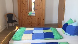 A bedroom with a wooden wardrobe, a bed with a checkered bedspread, and a chair. - Amber (1st floor left) - Villa Meeresrauschen (Zempin)