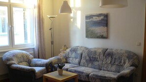 A living room with a patterned sofa, a small table, a potted plant, a floor lamp, and a painting on the wall. - Amber (1st floor left) - Villa Meeresrauschen (Zempin)