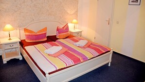 A neatly made bed with striped bedding, two bedside lamps, and a small bedside table with a drawer. - 04 Double Room - Villa in the Baltic Sea resort Baabe (Baabe)