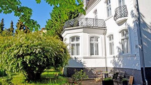 A white building with a balcony and a tree in the foreground. - 04 Double Room - Villa in the Baltic Sea resort Baabe (Baabe)