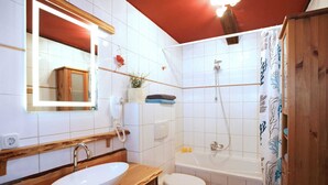 Un baño con tocador de madera, lavamanos blanco, inodoro y ducha.