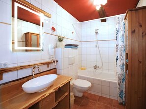 Une salle de bain avec un meuble-lavabo en bois, un lavabo blanc, des toilettes et une douche.