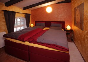 Une chambre à coucher avec un grand lit, deux lampes de chevet, une fenêtre avec des rideaux et un tableau au mur.