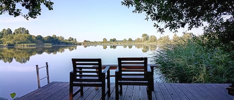 A wooden deck with two chairs facing a calm lake, surrounded by trees and vegetation.