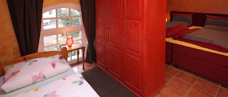 Un dormitorio con cama, un armario rojo, una ventana con cortinas y vistas al exterior.