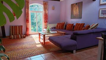 Ein Wohnzimmer mit einem violetten Sofa, einem gemusterten Teppich und einem großen Fenster mit Vorhängen.