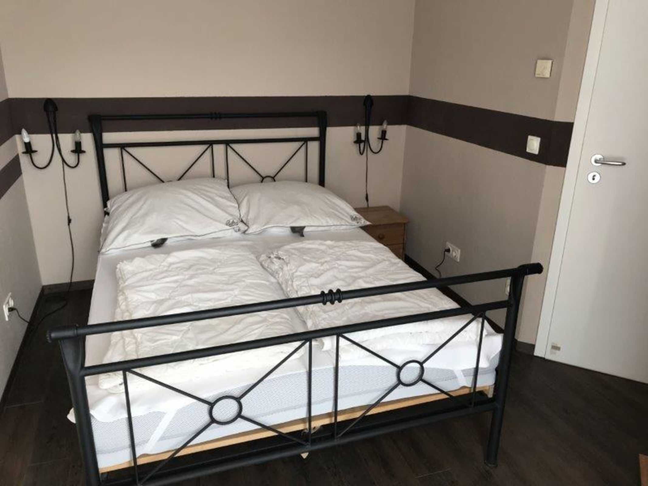 Ein Einzelbett mit schwarzem Metallgestell, weißer Bettwäsche und einem Nachttisch aus Holz daneben.