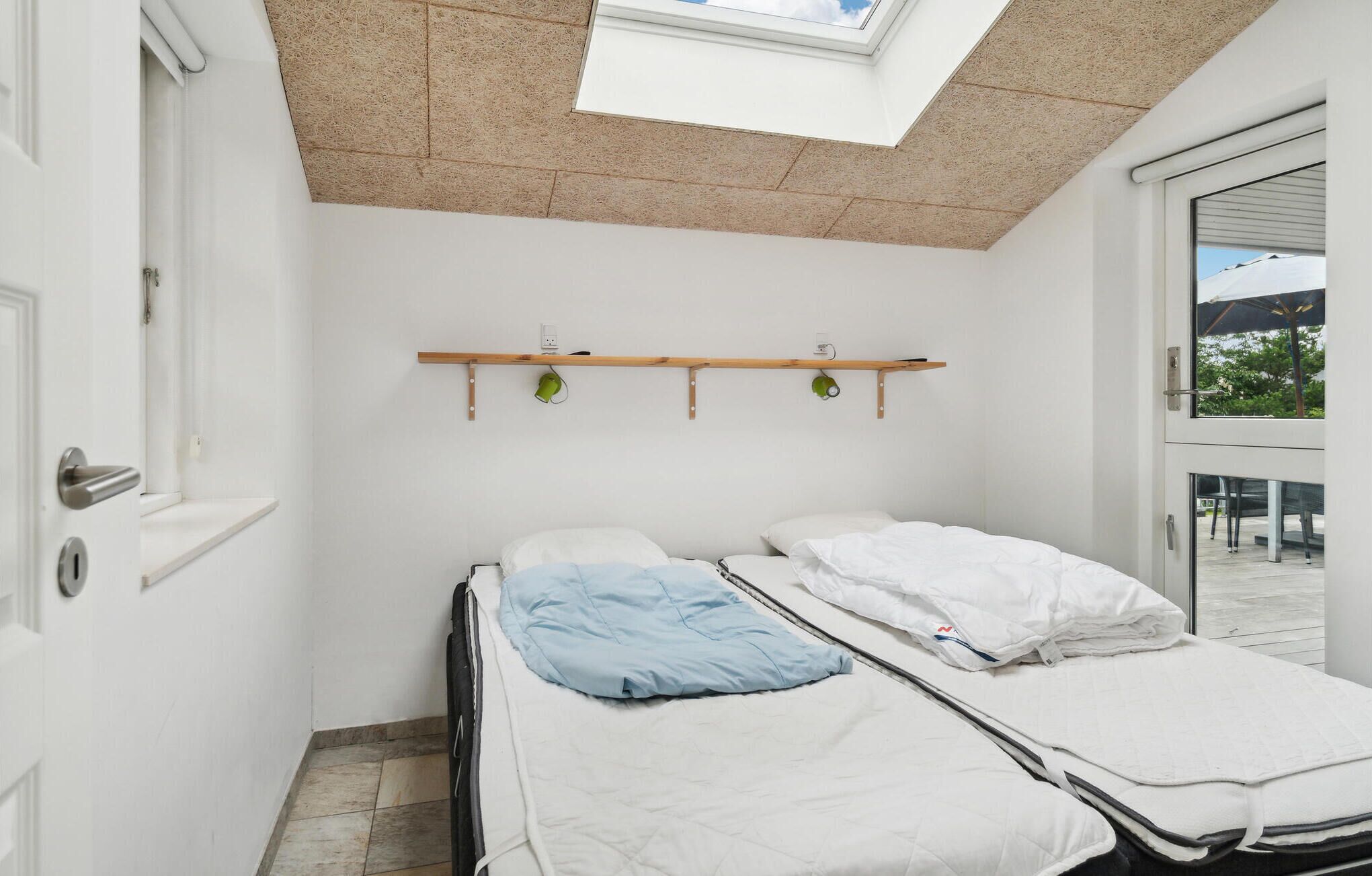 Una habitación pequeña y luminosa con tragaluz, una cama, una estantería con tazas y vistas al exterior.