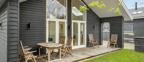 A wooden deck with a table and chairs, a glass door entrance, and a view of the sky.