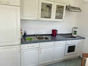 Een keuken met witte kastjes, een roestvrijstalen spoelbak, een rode waterkoker en een koffiezetapparaat.