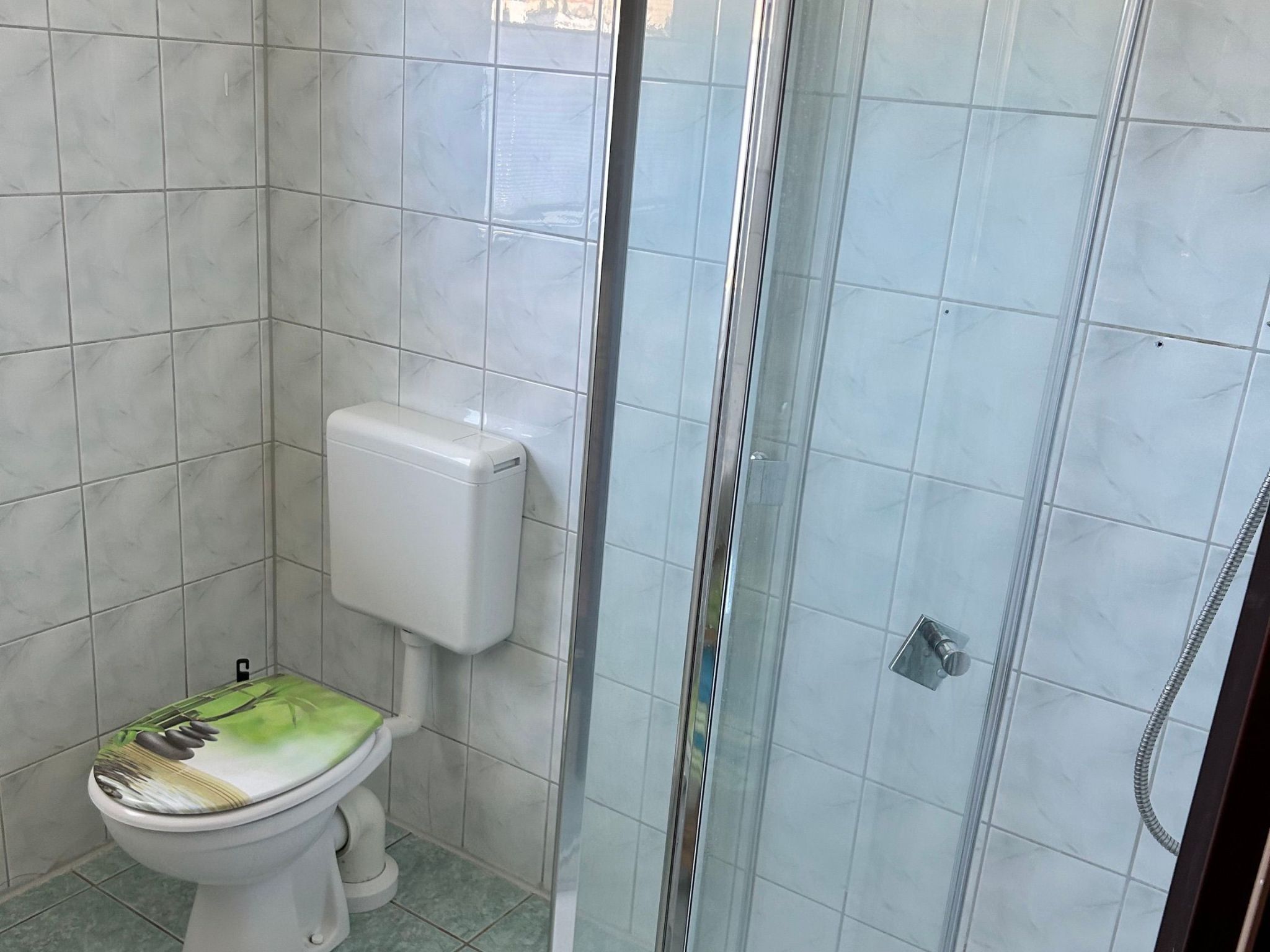 Une salle de bain avec des toilettes, une douche et des murs carrelés.