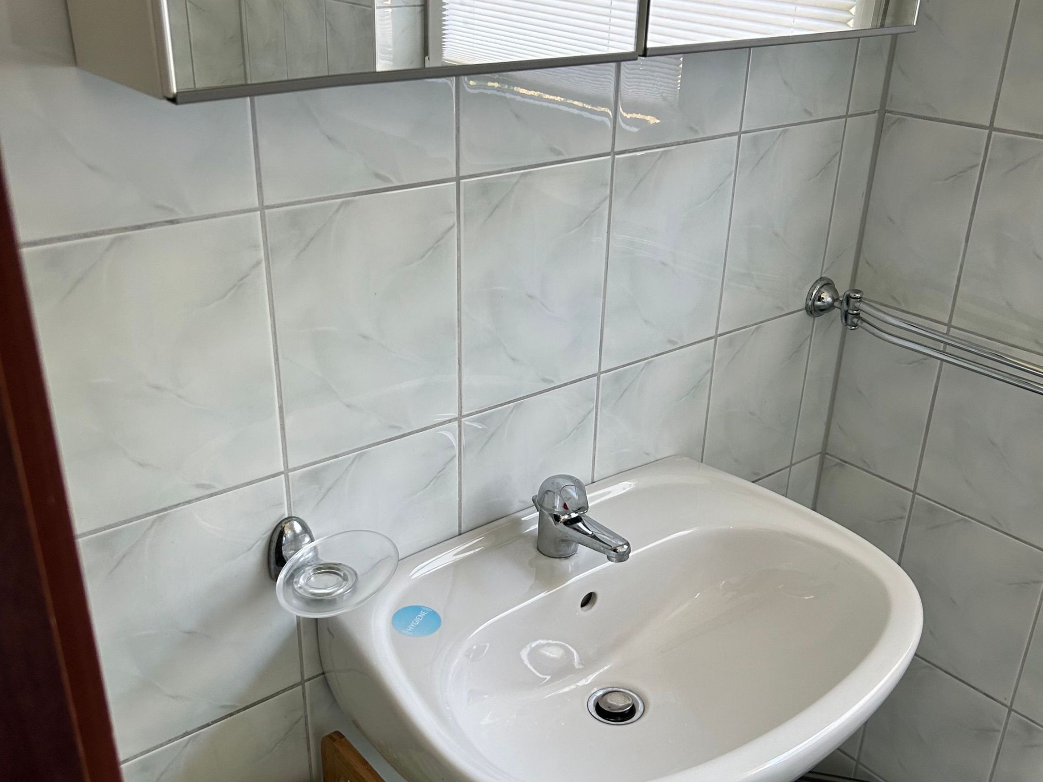 Een badkamer met een witte wastafel, een spiegel erboven en betegelde wanden.