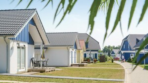 Eine Reihe moderner, eingeschossiger Häuser mit Ziegeldächern, einem Rasen und blauem Himmel.