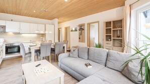 Ein modernes Wohnzimmer mit grauem Sofa, einem Couchtisch und einem Essbereich mit Stühlen und Tisch.