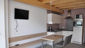 Une cuisine moderne avec des meubles blancs, un banc en bois, une table et un téléviseur fixé au mur.