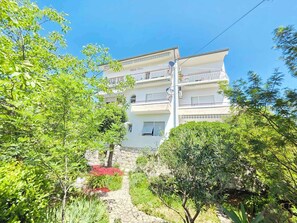 A multi-story building with balconies, surrounded by greenery and a stone pathway.