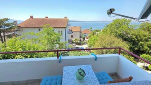 A balcony with a table, cushions, and a view of the sea and buildings.