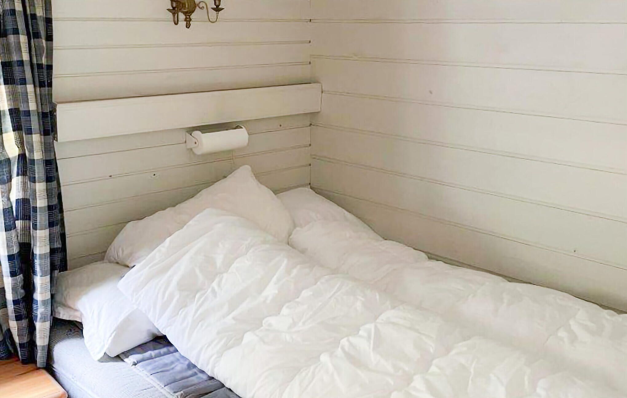 A single bed with white bedding in a room with wooden paneling and a curtain on the left.