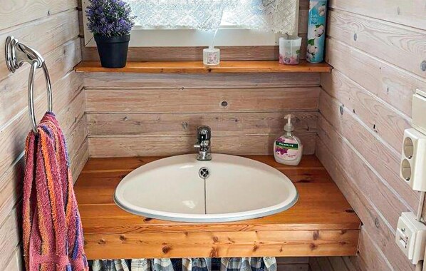 A wooden cabin bathroom with a white sink, a towel rack, a potted plant, and a window with lace curtains. - Stunning home in Farsund with ethernet internet (Farsund)