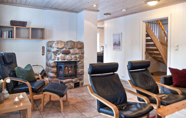 A cozy living room with a stone fireplace, leather chairs, a wooden coffee table, and a staircase leading upstairs.